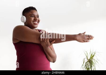 Motivierte übergewichtige schwarze Frau, die sich streckt und Musik hört Stockfoto