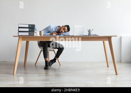 Erschöpfter Junger Mann Schläft Bei Der Arbeit Und Sitzt Am Schreibtisch Stockfoto
