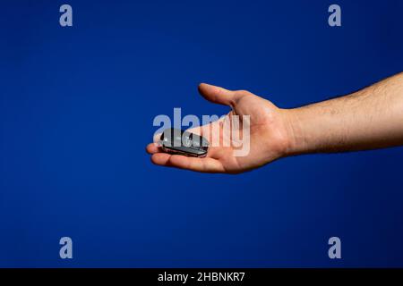 Die Hand des Mannes bietet großzügig seine Autoschlüssel an, isoliert auf blauem Studiohintergrund Stockfoto