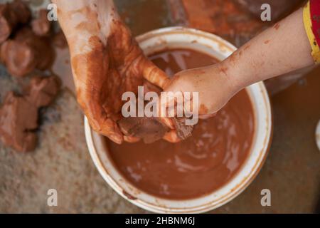 Frau hält einem Kind Ton, während er ihn formt. Stockfoto