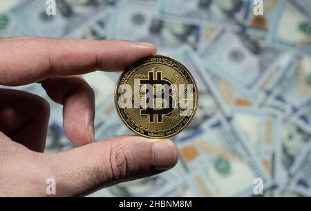 Männliche Hand hält Gold Bitcoin Münze, hundert Dollar-Scheine Hintergrund der Gold Bitcoin Münze. Stockfoto