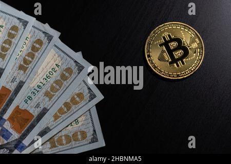 Gold glänzende Bitcoin Krypto-Währungsmünzen mit hundert US-Dollar-Scheinen auf schwarzem Hintergrund Stockfoto