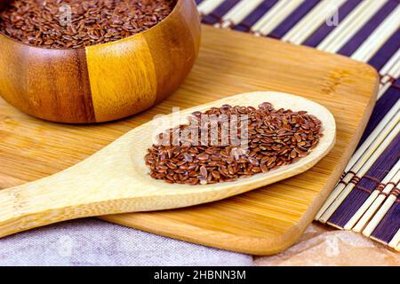 Braune rohe trockene Leinsamen in einem Holzlöffel auf hellem Textilhintergrund. Stockfoto