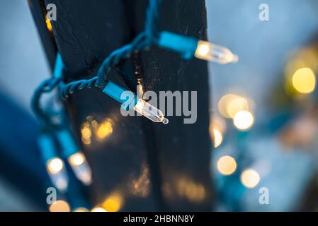 Dynamische Nahaufnahme von festlichen Lichterketten, die während der Weihnachtszeit um ein eisernes Tor mit einem blauen und gelben Hintergrund hingen Stockfoto