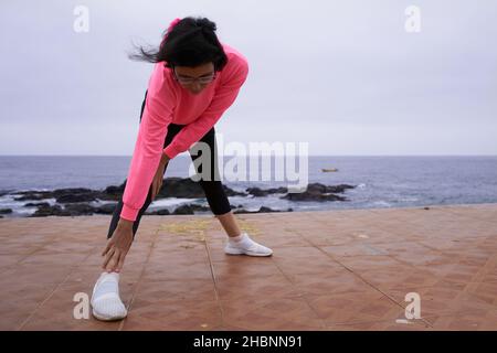 Junge Frau führt Dehnübungen vor dem Meer durch. Sport Stockfoto