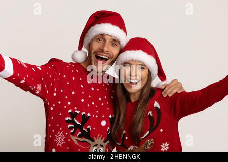 Fröhliches Junges Paar In Santa Hats Und Weihnachtslieder, Die Selfie Zusammen Nehmen Stockfoto