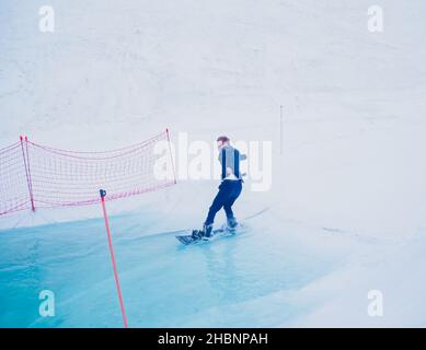 Russland, Sotschi 11.05.2019. Ein Typ in einem Business-Anzug, der eine Brille trägt, fährt ein Snowboard und überwindet ein Hindernis mit Wasser. Wettbewerbe Krasnaya Polyana Stockfoto