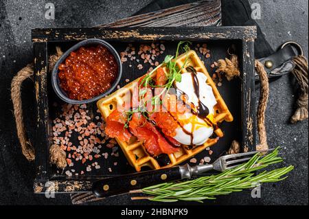 Köstliche Waffeln mit geräuchertem Lachsfilet, pochiertem Ei und rotem Kaviar. Schwarzer Hintergrund. Draufsicht Stockfoto