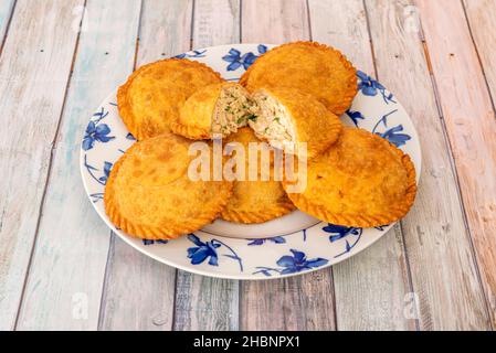 Empanadas gefüllt mit gezogenem Hühnerfleisch mit Petersilie auf weißem Teller und blauen Blüten Stockfoto