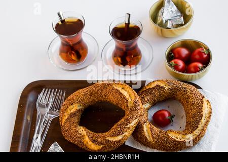 Snack-Frühstück mit knusprigen, frischen, traditionellen türkischen Bagel Simit, Kirschtomate, türkischem Tee und Dreieckscreme-Käse auf dem Holztablett Stockfoto