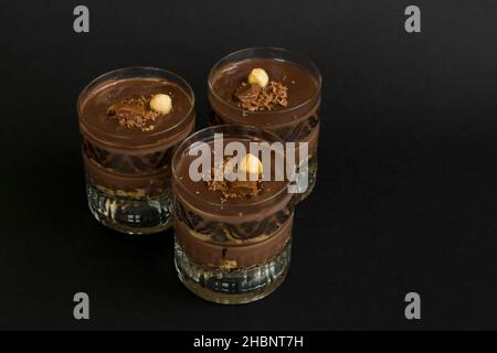 Kakaopuldding Dessert mit Keksen in Staylish Gläser auf schwarz geschichtet.garniert mit Nuss und Schokolade. Stockfoto