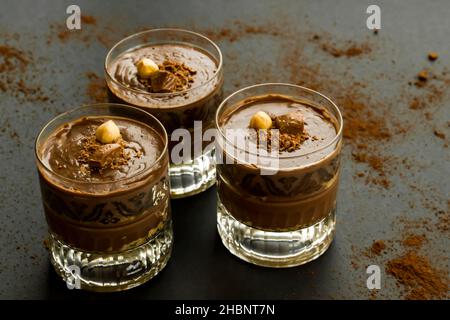 Kakaopuldding Dessert mit Keksen in Staylish Gläser auf schwarz geschichtet.garniert mit Nuss und Schokolade. Stockfoto