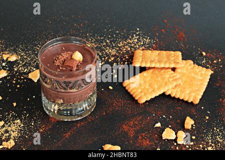 Kakaopuldding Dessert mit Keksen in Staylish Gläser auf schwarzer Oberfläche mit Keksen geschichtet.garniert mit Nuss und Schokolade. Stockfoto