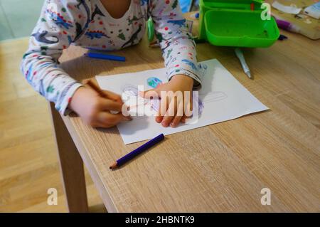 POZNAN, POLEN - 06. Apr 2019: Ein kleiner Junge zeichnet etwas auf weißem Papier an einem Holztisch. Stockfoto