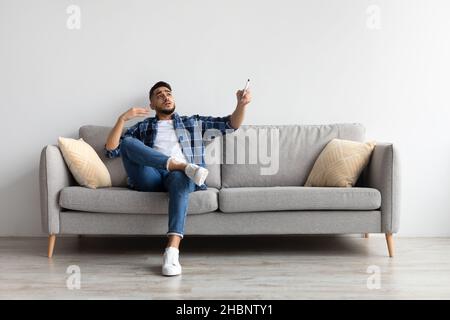 Junger Mann, der zu Hause die Klimaanlage anschaltet Stockfoto