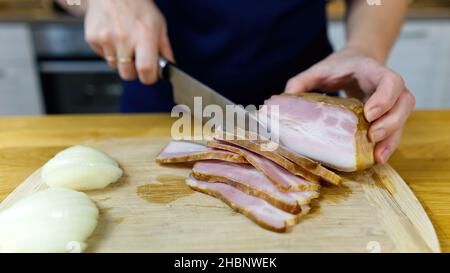 Cook schneidet Speck auf einem Holzbrett Stockfoto