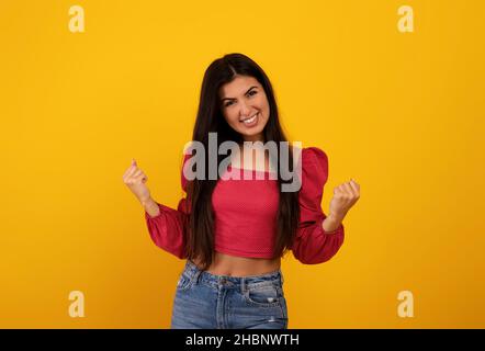 Überglücklich armenische Frau, die ja gestikulierte, Erfolg oder Erfolg feierte und auf gelbem Studiohintergrund posierte Stockfoto