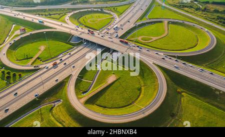 Luftaufnahme einer Kreuzung von Autostraßen mit Brücken und Lastwagen und Autos an einem sonnigen Tag vor einem grünen Rasen Stockfoto