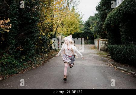 Mädchen, die im Herbst in Großbritannien fröhlich durch die Straßen Rennen Stockfoto