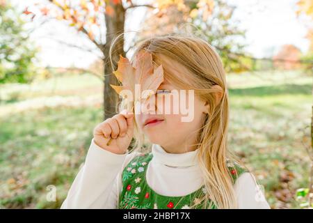 Nahaufnahme eines jungen Mädchens, das mit einem Herbstblatt spielt Stockfoto