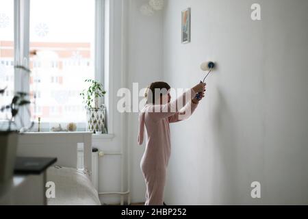 Das Kind malt eine weiße Wand im Zimmer. Stockfoto