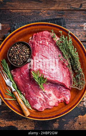 Zwei Lappen oder Flanken rohes Rindfleisch Steaks auf einem rustikalen Teller mit Kräutern. Dunkler Holzhintergrund. Draufsicht Stockfoto