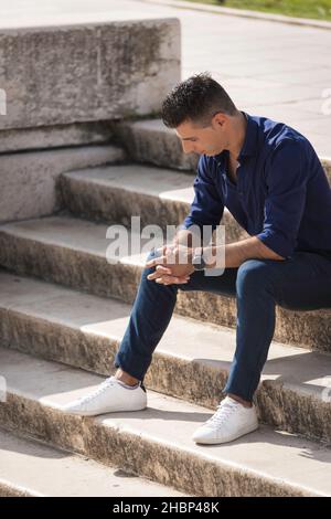 Ein freiberuflicher Architekt, der allein auf der Betontreppe im Herzen von Lissabon sitzt, sich entspannt und eine Pause von der Arbeit macht. Nobler junger Unternehmer wir Stockfoto