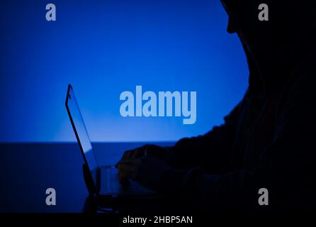 Eine Nahaufnahme der Silhouette einer Person in einer Kapuze, die an einem Computer arbeitet - Hacking-Konzept Stockfoto