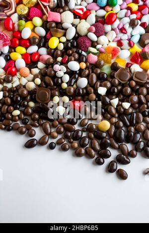 Bunte Bonbons und dunkle Schokoladenkugeln auf der weißen Oberfläche mit Kopierraum gemischt, vertikales Bild Stockfoto