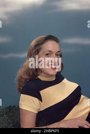 Junge Frau in schwarz-gelb gestreifter Bluse, die lächelnd auf die Kamera blickt, während sie im Gras liegt Stockfoto