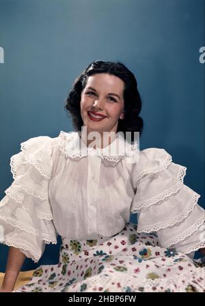 Junge Frau Porträt trägt weiße Bluse und Blumendruck Kleid steht vor einem blauen Hintergrund Stockfoto