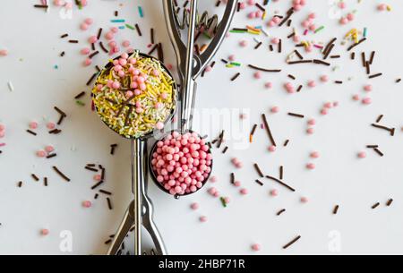 Bunte streut Zuckerstränge, Vermicelli-Kuchen, Cupcake-Dekorationen auf der weißen Oberfläche und in zwei Eisschaufeln.Konzeptuelles Bild des Konditors Stockfoto