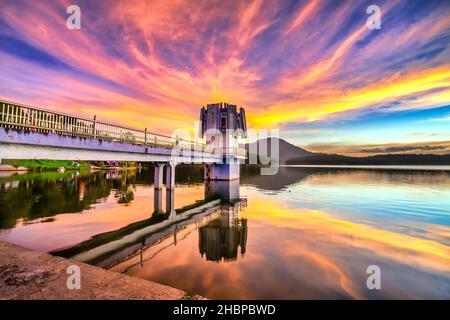 Die leuchtenden Farben des Sonnenuntergangs am Seeufer, wo sich der Wasserkraftdamm befindet, locken viele Besucher an Wochenenden zum Entspannen an Stockfoto