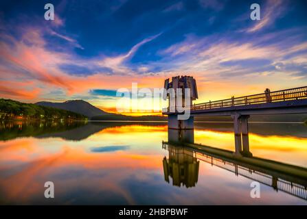 Die leuchtenden Farben des Sonnenuntergangs am Seeufer, wo sich der Wasserkraftdamm befindet, locken viele Besucher an Wochenenden zum Entspannen an Stockfoto