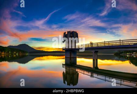 Die leuchtenden Farben des Sonnenuntergangs am Seeufer, wo sich der Wasserkraftdamm befindet, locken viele Besucher an Wochenenden zum Entspannen an Stockfoto