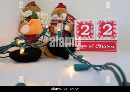 22 Tage bis Weihnachten Countdown-Kalender aus Holzblöcken auf einem Mantel mit Lichtern und einem Plüsch Spielzeug Schneemann. Stockfoto