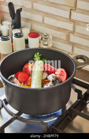 Fischbarsch wird im Kessel mit Tomaten, Karotten und Zwiebeln auf dem Gasherd geschmort Stockfoto