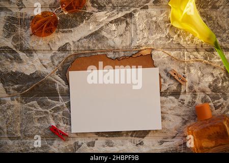 Vintage-Stil aus imitiertem Papier und Briefpapier-Karte für Einladung oder Herzlichen Glückwunsch. Orange Parfüm Flakon und Sonnenbrille. Dekorationen aus gelber Calla-Blume. Feminines, ästhetisches Konzept. Backsteinkulisse Stockfoto