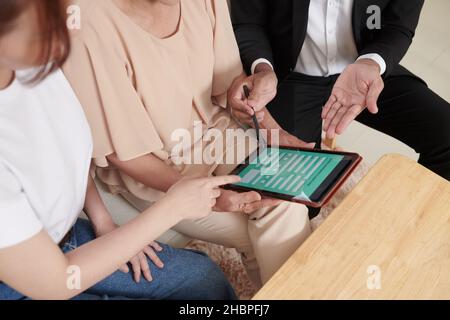 Hände von Krankenkassen, die den Kunden das Formular auf einem Tablet-Computer zeigen, den sie mit persönlichen Daten füllen Stockfoto