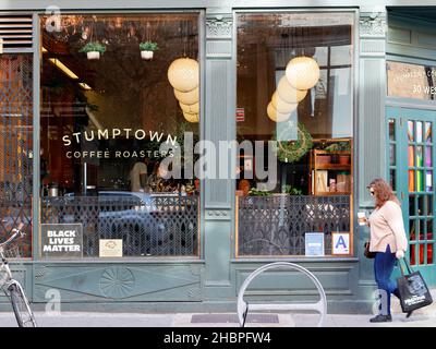 Eine Frau mit einer Starbucks Tasse Kaffee geht an einem Stumptown Coffee Roasters in New York, NY, vorbei. Stockfoto