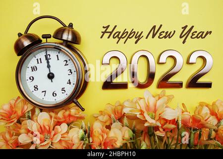 Frohes neues Jahr 2022 Text mit Wecker und Blumendekoration auf gelbem Hintergrund Stockfoto