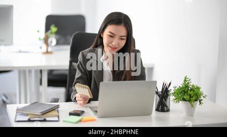 Konzentrierte asiatische Geschäftsfrau mittleren Alters, die eine E-Mail liest und im Büro an ihrem Laptop arbeitet. Stockfoto