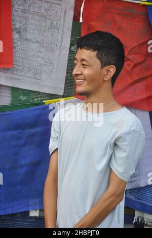 Foto eines asiatischen jungen Mannes, der lächelt und seitwärts schaut, der gegen buddhistische Gebetsfahnen mit Kopierraum steht Stockfoto