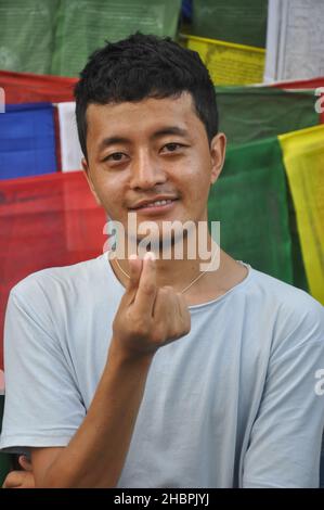 Nahaufnahme eines glücklichen Tibets, der mit der Hand ein koreanisches Liebeszeichen macht, während er die Kamera anschaut und sich gegen buddhistische Gebetsfahnen posiert Stockfoto