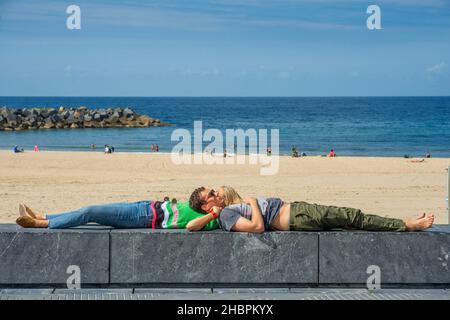 Ein romantisches Paar mit Blick auf den schönen, aber überfüllten Playa de La Concha (Strand von Zurriola) in San Sebastián (Donostia), Spanien. Strand von Playa de Stockfoto