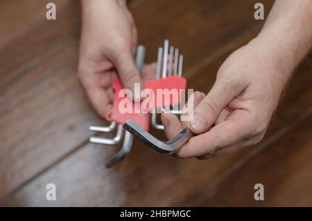 Hände halten einen Satz Sechskantschlüssel gegen den braunen Holzboden. Ein erwachsener Mann mit einem Handwerkzeug. Blick von oben aus einem Winkel. Selektiver Fokus. Stockfoto