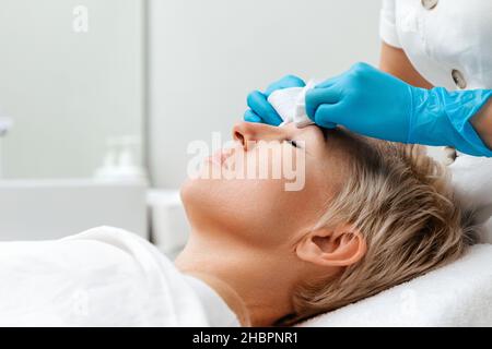 Professionelle Betreuung im Schönheitssalon. Der Kosmetologe führt eine tiefe mechanische Reinigung des Gesichts des Kunden durch. Seitenansicht. Akne-Konzept. Stockfoto