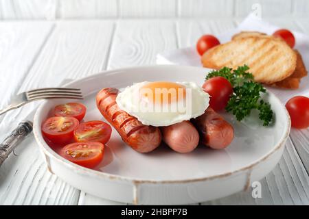 Spiegeleier mit Würstchen, Tomaten und Toast auf weißem Holzhintergrund Stockfoto
