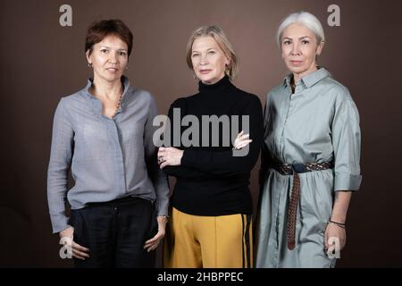 Porträt von älteren Frauen in eleganten Kleidern, die vor der Kamera lächeln, während sie vor dem grauen Hintergrund stehen Stockfoto