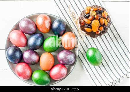 Draufsicht auf einen großen Festteller mit bunt bemalten Eiern zu Ostern. Ein dekorierter Osterkuchen auf Serviette. Weißer Hintergrund Stockfoto